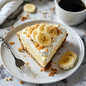 A slice of banana pudding cheesecake on a white plate, topped with whipped cream and banana slices, with a cup of coffee nearby.