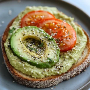 Avocado hummus toast topped with fresh avocado slices, tomato slices, sesame seeds, and herbs, served on a rustic plate.