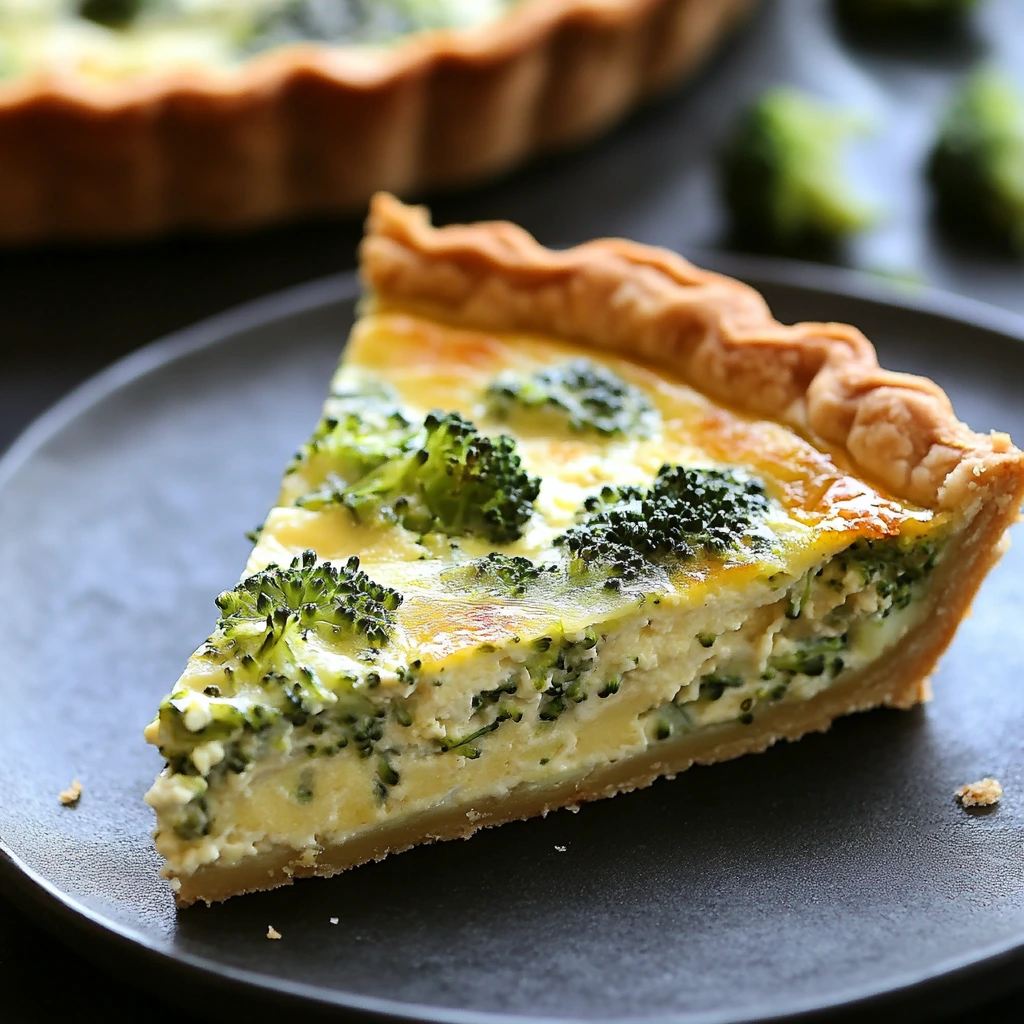 A slice of green goddess broccoli quiche with a golden, flaky crust and topped with fresh herbs, served on a modern plate